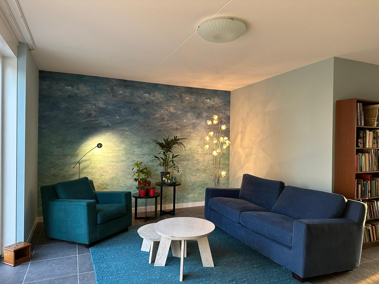 Moderne woonkamer met blauwe bank en artistieke muurschildering met renovlies.
